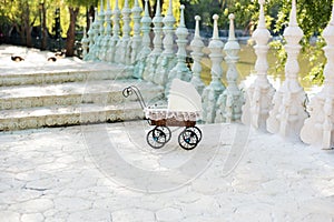 Doll's pram. Vintage doll stroller placed on the stairs to a beautiful lake. Retro cart dolls made of rattan and white lace.