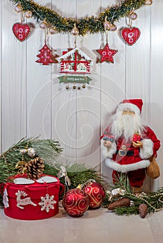 Doll Santa Claus, New Year`s decor, garland, Christmas tree branches and a gift in a round red box. Happy New Year mood. Vertical.