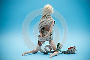 Doll wrapped in measuring tape on blue background -  female fight for a perfect body - Dieting concept