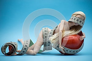 Doll wrapped in measuring tape with tomato on blue background -  female fight for a perfect body - Dieting concept