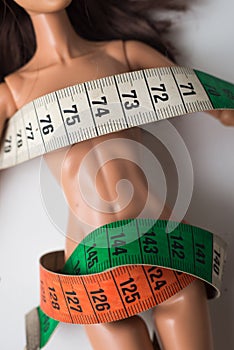 Doll wrapped in measuring tape on white background - female fight for a perfect body - Dieting concept