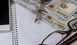 Dollar banknotes, closeup lie on a white sheet of paper next to a pen and glasses in a plastic frame