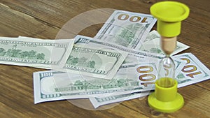 Dollar Banknotes Falling on a Wooden Table and Hourglass