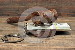 Dollar banknotes, handcuffs and judge gavel on wood table