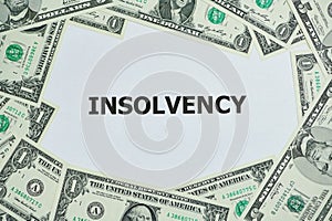 Dollar banknotes lying around the word insolvency printed on a white paper