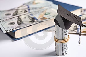 Dollar banknotes with mini student graduation hat and book on background. Tuition fees concept