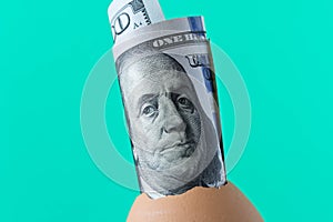 100 dollar bill in an egg shell. On a turquoise background. The
