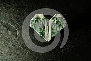 Dollar bill origami heart shape on dark textured background