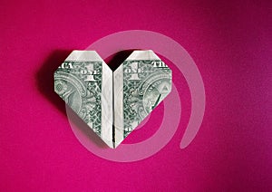 Dollar bill origami heart shape on pink textured background