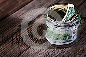 Dollar bills in glass jar on wooden background. Saving money concept