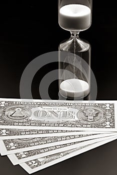 Dollar bills lie near the hourglass. Time is money. The salary. Business solutions in time. Hourglass time measurement