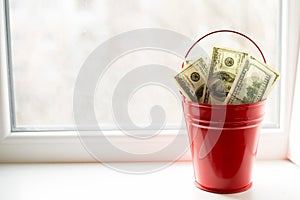 Dollar bills in red pail. on white window.light background. place for text. top view. a lot of money