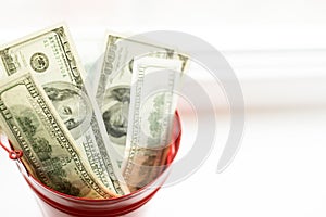 Dollar bills in red pail. on white window.light background. place for text. top view. a lot of money