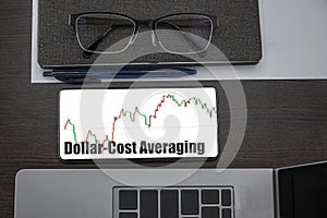 Dollar-Cost Averaging investment. Top view of stocks price candlestick chart in phone on table near laptop, notepad and glasses