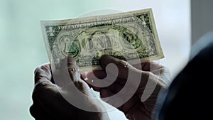 Dollar in hand. View against the window, hands holding a dollar. Currency paper money, bill in hand.