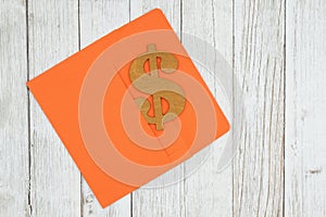 Dollar sign symbol with orange envelope on textured weathered whitewash wood background