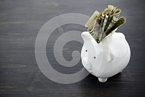 Dollars banknotes money into piggy bank on wooden background. Saving money and financial concept.