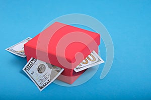 Dollars banknotes are stuck out of a red gift box on a blue background