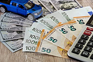 Dollars, euros, a calculator and a toy blue car on a wooden background