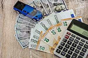 Dollars, euros, a calculator and a toy blue car on a wooden background