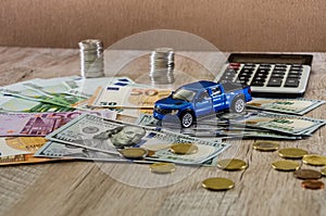 Dollars, euros, coins, a calculator and a toy blue car on a wooden background