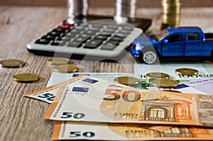 Dollars, euros, coins, a calculator and a toy blue car on a wooden background