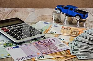 Dollars, euros, coins, a calculator and a toy blue car on a wooden background