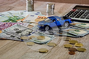 Dollars, euros, coins, a calculator and a toy blue car on a wooden background