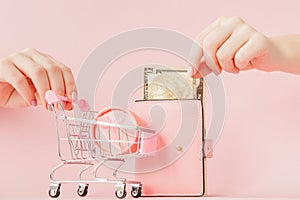 Dollars, gift box and pink wallet with credit card in woman`s hands on pink background