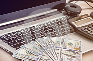 Dollars on laptop keyboard, calculator and headphones. Close-up .