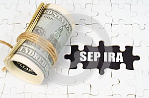 Dollars lie on white puzzles, on a black surface there is an inscription - SEP IRA