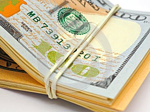 Dollars lies on a white paper background. Above - a hundred-dollar bill of new sample. Fragment close-up. The bundle is rolled up