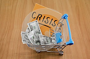 Dollars in a shopping cart and a sticker with the words `crisis`. The concept of economic crisis. Drops in income and solvency.