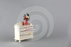 Dollhouse interior - vase of flowers on old-fashiobed white commode isolated on gray background