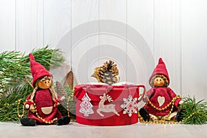 Dolls, New Year`s decor, branches of a Christmas tree and a gift in a red round box on a light wooden. Merry New Year mood.