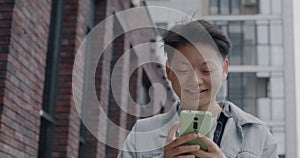 Dolly shot of cheerful Asian man using smartphone chatting in social media walking in urban street