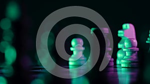 Dolly shot of chess pieces on wooden chessboard under neon colorful light - pink and green. Board strategy game