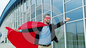 Dolly shot of entrepreneur in superman costume cape and mask running outdoors