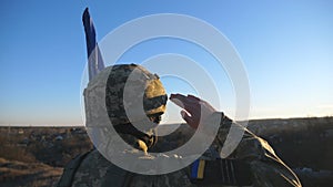 Dolly shot of male ukrainian army soldier with blue-yellow banner saluting against of sunset. Young military man in