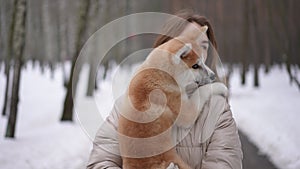 Dolly shot portrait of smiling confident young woman with dog in hands walking outdoors looking around. Front view