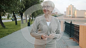 Dolly shot of senior woman walking outside in modern city street smiling looking at river