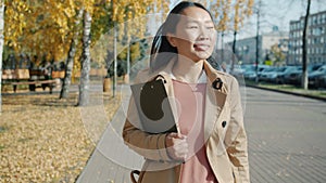 Dolly shot of young attractive Asian lady walking outside in urban streen smiling carrying papers