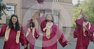 Dolly shot of young people students running on campus throwing mortar boards celebrating graduation