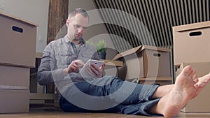 Dolly shot of young smiling man moving to a new house and using digital tablet