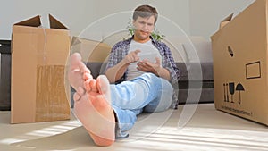 Dolly shot of young smiling man moving to a new house and using digital tablet