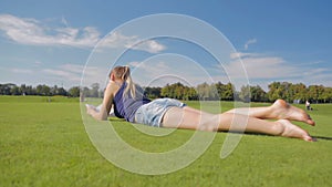 Dolly shot of young student girl lying on grass at park and reading a book