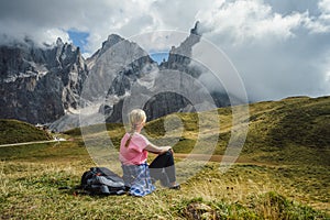 Dolomites. Woman sitting on the grass enjoying Baita Segantini mountain with Cimon della Pala peak, refuge and lake in