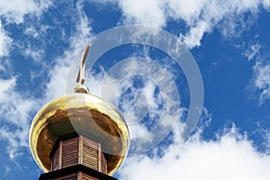 The dome of the Church with a cross on the sky background with white clouds.