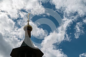 The dome of the Church with a cross on the sky background with white clouds.