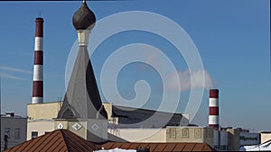 The dome with the cross of the Orthodox church on the background of the pipes of the chemical industry factory.